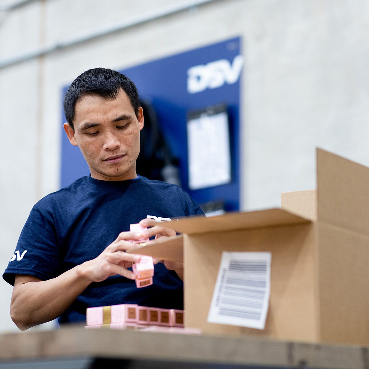 DSV:n työntekijä sinisessä paidassa pakkaa kosmetiikkatuotteita ruskeaan pahvilaatikkoon.